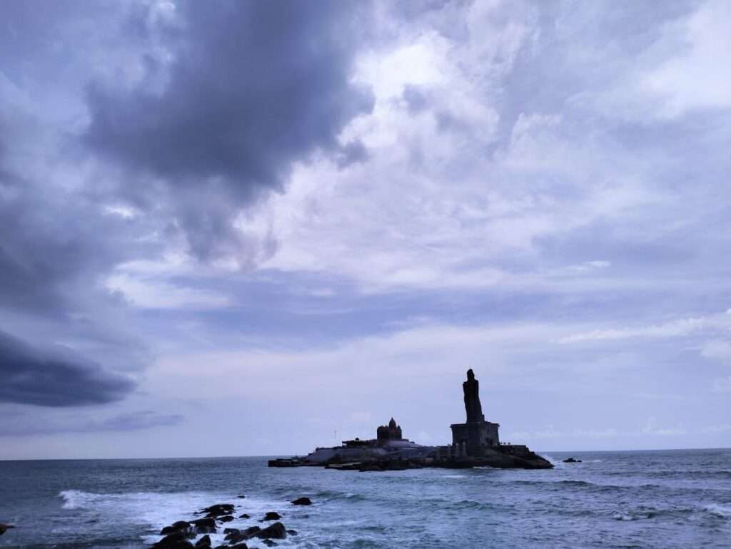 A cloudy blue sky and a view of Kanyakumari from the shore.
