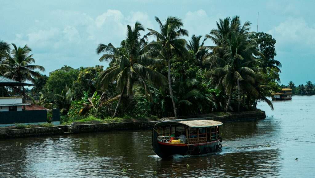 A small boat with passengers is moving in the backwaters of Alappuzha and the nature is very beautiful with all the coconut trees around the backwaters.